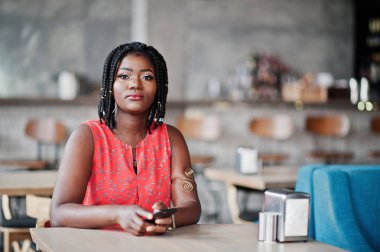 Çekici Afrikalı-Amerikalı kadın elinde cep telefonu ile kafe üzerinde masada oturan.