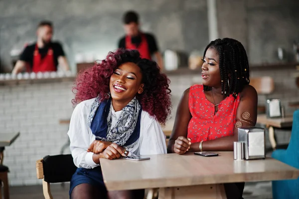 Attractive african american two girls friends sitting at table on cafe with mobile phones.