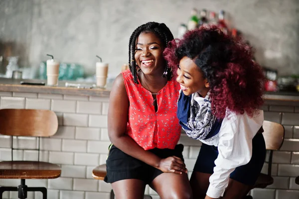 Attractive african american two girls friends sitting at chairs against bar on pub.