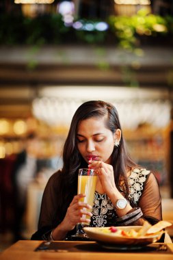 Restoranda, suyu ve salata ile masada oturan siyah sari giysili güzel Hintli kız poz.