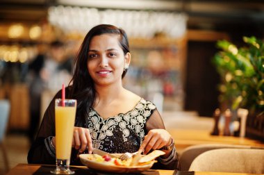 Restoranda, suyu ve salata ile masada oturan siyah sari giysili güzel Hintli kız poz.