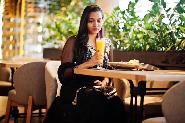 Restoranda, suyu ve salata ile masada oturan siyah sari giysili güzel Hintli kız poz.