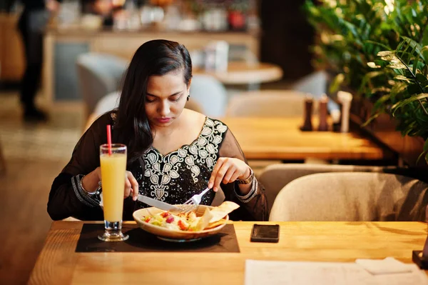 Restoranda, suyu ve salata ile masada oturan siyah sari giysili güzel Hintli kız poz.