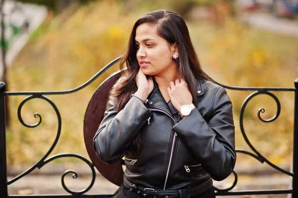 漂亮的印度女孩在黑色萨里礼服和皮夹克摆在户外在秋天的街道和坐在长凳上 — 图库照片