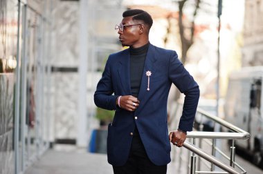 İnanılmaz Afro-Amerikan erkek giyimi mavi ceket broş ile seyir, siyah boğazlı kazak ve gözlük Sokağı'nda poz verdi. Şık siyah adam.