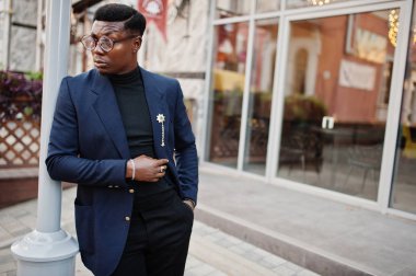 İnanılmaz Afro-Amerikan erkek giyimi mavi ceket broş ile seyir, siyah boğazlı kazak ve gözlük Sokağı'nda poz verdi. Şık siyah adam.