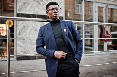 İnanılmaz Afro-Amerikan erkek giyimi mavi ceket broş ile seyir, siyah boğazlı kazak ve gözlük Sokağı'nda poz verdi. Şık siyah adam.