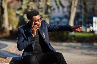 İnanılmaz Afro-Amerikan erkek giyimi mavi ceket broş ile seyir, siyah boğazlı kazak ve gözlük Sokağı'nda poz verdi. Şık siyah konuşan adam ve bir şey göstermek.