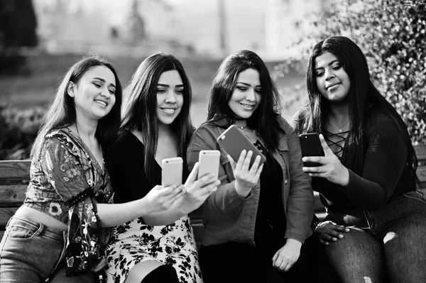 Group of four happy and pretty latino girls from Ecuador posed at street and looking at mobile phones.