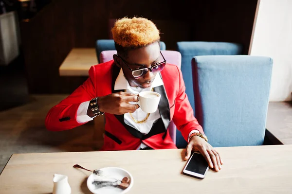 Fashion african american man model at red suit, with highlights hair and sunglasses sitting at cafe with coffee.
