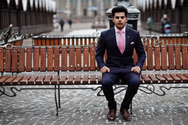 Takım elbise ve kış gününde poz ve bankta oturan Pembe kravat zarif Hint maço erkek modeli.