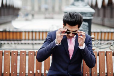 Zarif Hint maço erkek model takım elbise ve pembe kravat, kış gününde poz ve bankta oturan güneş gözlüğü.