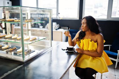 Sarı dreess şık Afrikalı-Amerikalı kadın Café fincan cappuccino ile poz verdi.