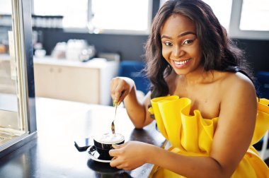 Sarı dreess şık Afrikalı-Amerikalı kadın Café fincan cappuccino ile poz verdi.