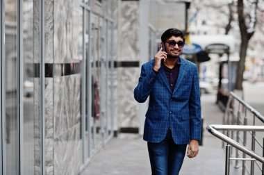 Açık ve telefonda konuşan genç Hintli takım elbise ve güneş gözlüğü üzerinde yarattığı.