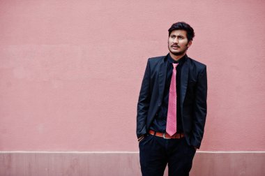 Takım elbise ve kravat üzerinde genç Hintli adam pembe duvara poz verdi..