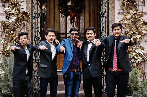 Group of 5 indian students in suits posed outdoor and show fingers.