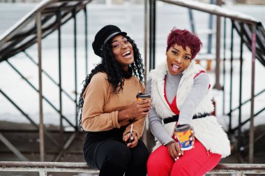 Kış günü bardak kahve ile karlı arka plan karşı iki Afrikalı-Amerikalı kadının poz.