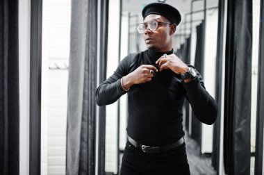 Aynaya bakarak şık rahat Afro-Amerikan adam siyah kıyafet ve bere ile Oda Giyim Mağazası, uydurma, bel çantası.