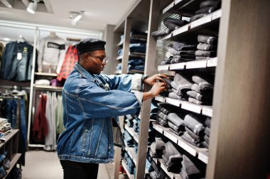 Şık casual Afro-Amerikan erkek kot ceket ve pantolon raflar üzerinde seyir giyim mağazasında siyah bere.