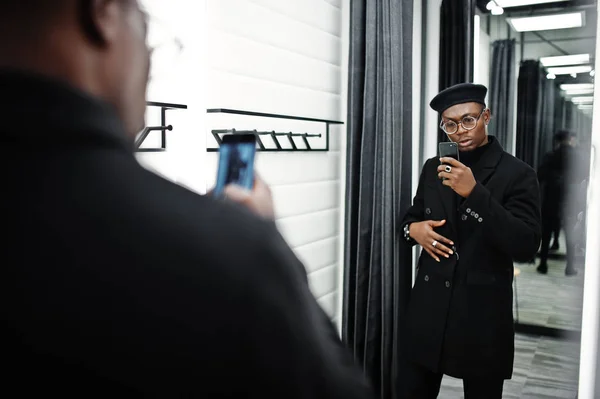 スタイリッシュなカジュアルなアフリカ系アメリカ人黒いベレー帽とフィッティング ルーム服店でコートでミラーで彼の携帯電話のカメラで写真を作る — ストック写真