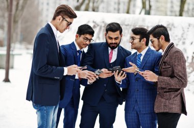 Takım elbiseli beş Hintli işadamı grubu Avrupa telefonları ve disscus bakarak, kış günü açık poz.
