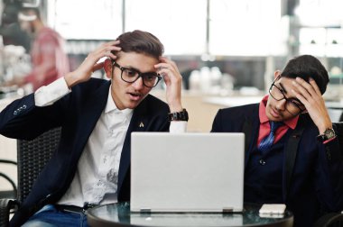 Ofiste kafe üzerinde oturan ve laptop arıyorum takım elbiseli iki Hint iş adamı. Hayal kırıklığına uğramış surat.