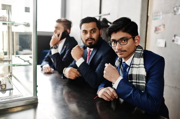 Group of three indian businessman in suits sitting on cafe.