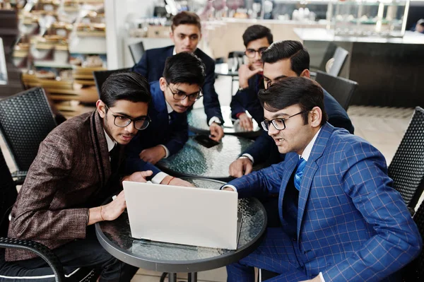 Group of six indian business man in suits sitting at office on cafe and looking at laptop.