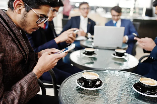 Group of indian business man in suits sitting at office on cafe with laptop, texting on phones and making photo of coffee.