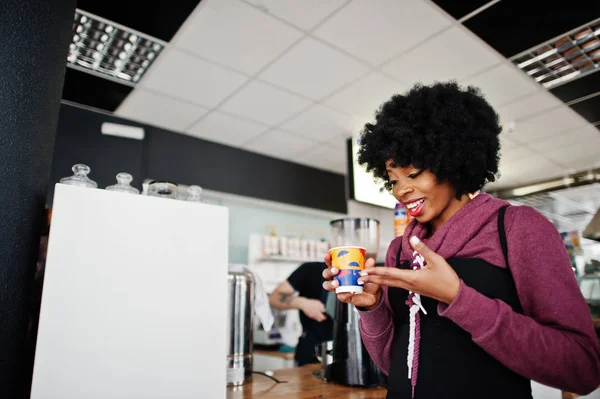 Curly hair african american woman wear on sweater posed at cafe indoor with cup of tea or coffee.