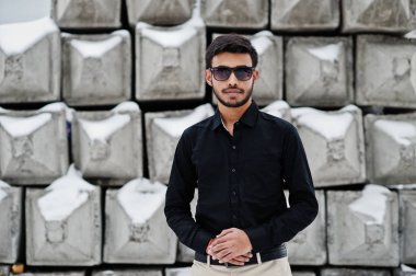 Siyah gömlek ve güneş gözlüğü rahat Hint delikanlı karşı taş bloklar poz verdi..