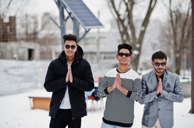 Kış gününde, gösterir namaste Hint içinde güneş gözlüğü mans üç sıradan genç grup poz.