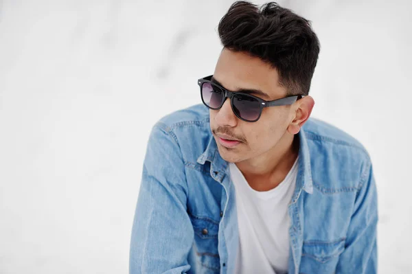 Casual young indian man in blue jeans shirt and sunglasses posed at winter day.