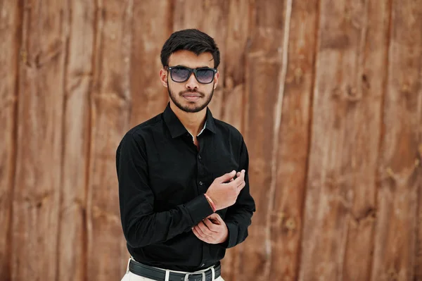 黒いシャツとサングラスでカジュアルな若いインド人が木製の背景に対して提起 — ストック写真
