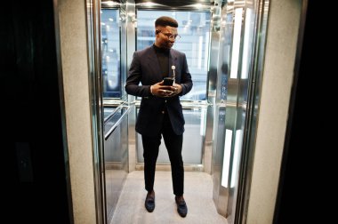 Moda Afro-Amerikan erkek takım elbise ve gözlük ile cep telefonu ve fincan kahve elinde Asansör içinde poz verdi..