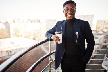 Moda Afro-Amerikan erkek takım elbise ve balkon ofisinde üzerinde yarattığı elinde kahve Kupası ile gözlük.