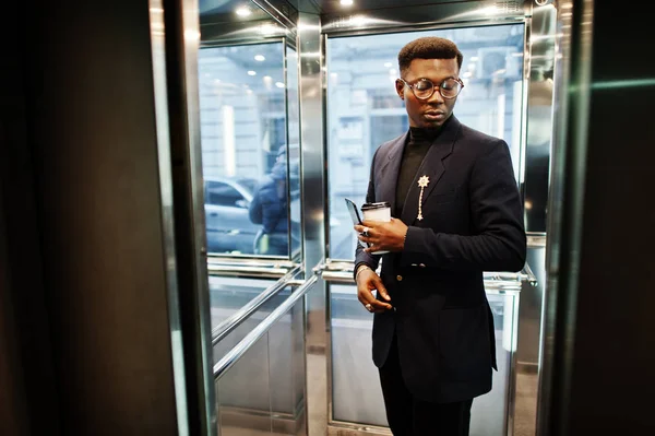 スーツと携帯電話 エレベーター内部脅威の手でコーヒー カップを持つガラスでおしゃれなアフリカ系アメリカ人 — ストック写真