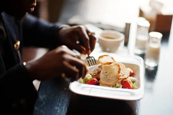 Close up hands of fashionable african american man in suit sitting at cafe and eating salad.