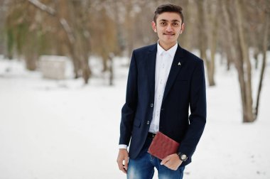 Takım elbiseli şık Hint öğrenci adam kış gününde açık elinde defter ile poz verdi.