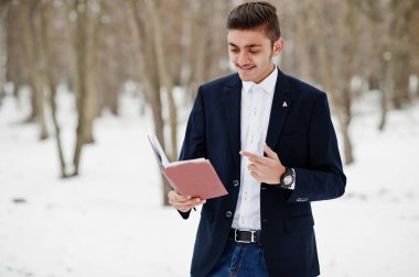 Takım elbiseli şık Hint öğrenci adam kış gününde açık elinde defter ile poz verdi.