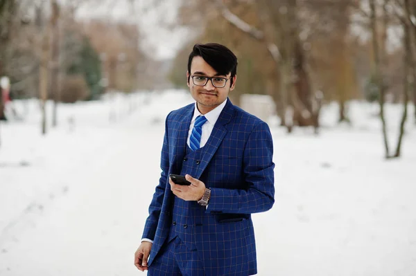 Stylish indian business man in suit and glasses posed at winter day outdoor, with mobile phone at  hand.