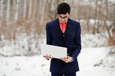 Şık Hint öğrenci erkek takım elbise ve gözlük kış günü açık dizüstü bilgisayar, el ile poz verdi.