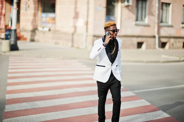 Chic handsome african american man in white suit walking on crosswalk and speaking on phone.