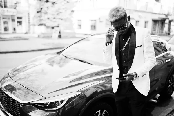 手元の携帯電話で赤い高級車に対して白いスーツでシックなハンサムなアフリカ系アメリカ人 — ストック写真