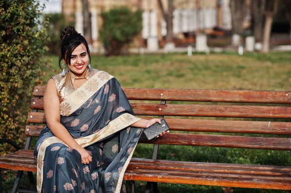 优雅的黑发南亚印度女孩在萨里坐在长凳上与手机在手 — 图库照片