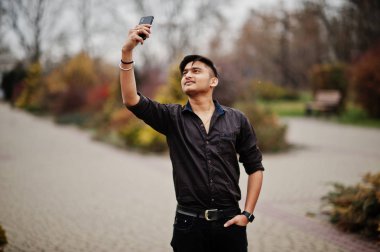 Kahverengi gömlekli Hintli adam cep telefonu açık ve yapım selfie poz verdi..