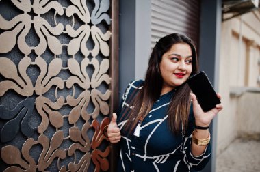 Uzun şık elbiseli esmer Hintli kadın açık cep telefonu el ile poz verdi.