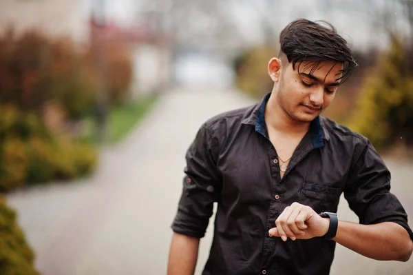 Indian man in brown shirt posed outdoor and looking at his watches.