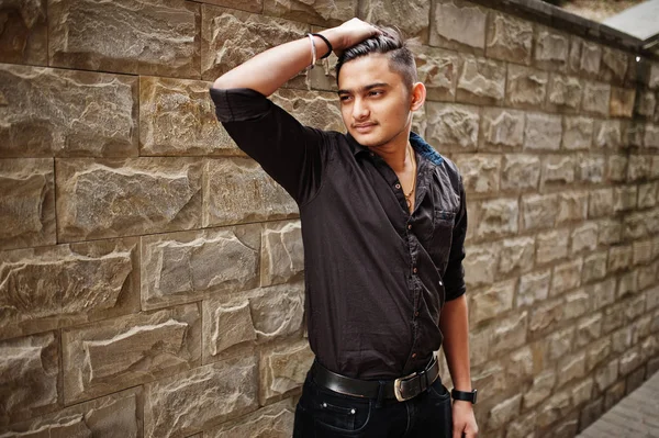 Indian man in brown shirt posed outdoor against brick background.